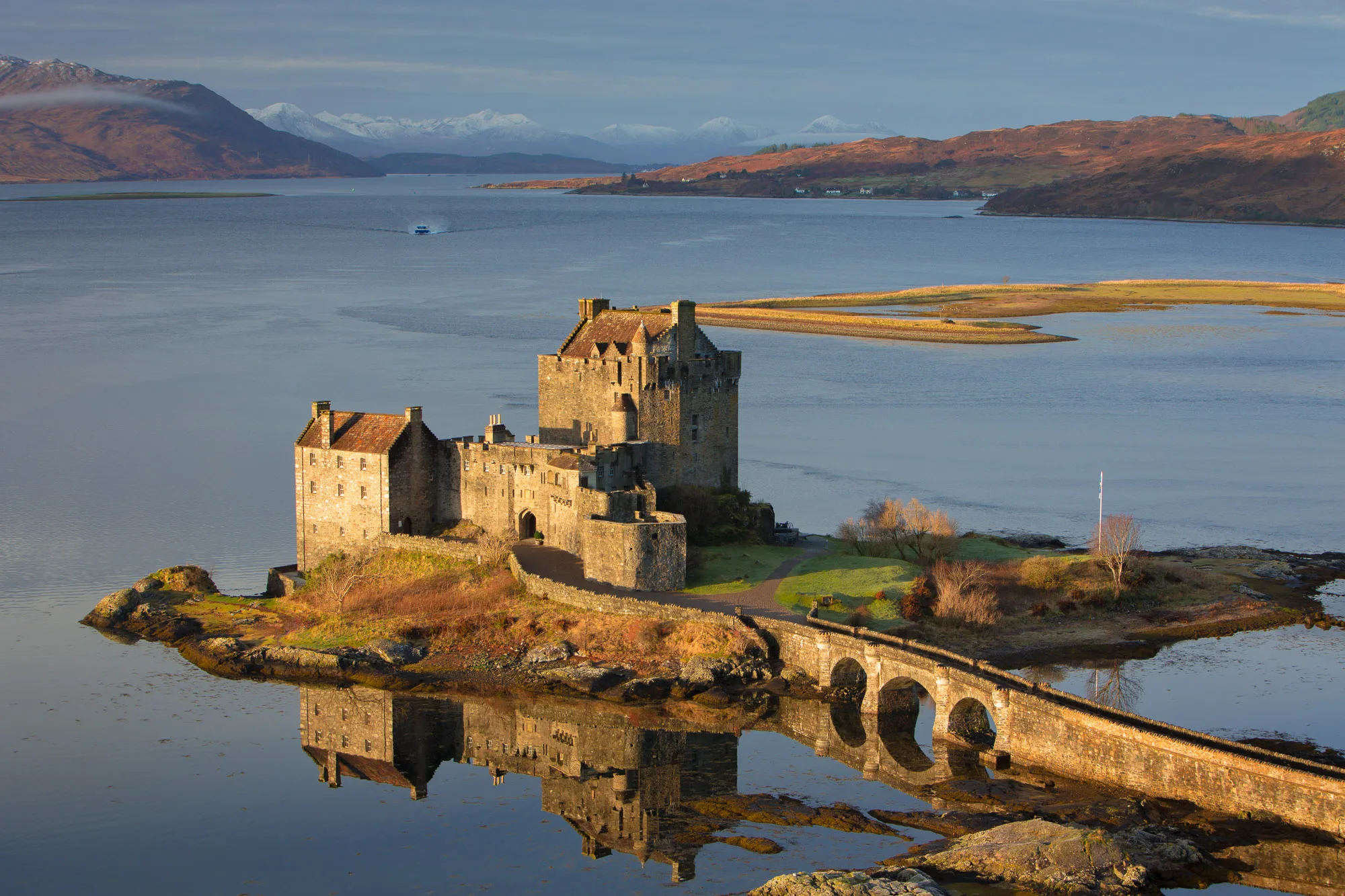 Eilean Donan Castle illumninted by early monring light. Scottish Landscape Photography with Loch, mountains and snow